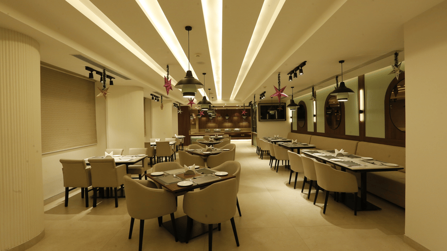  An image of a restaurant featuring several sets of tables, chairs, and sofa, lights hanging from the ceiling and mirrors attached on the wall at Tulip Inn, Zirakpur