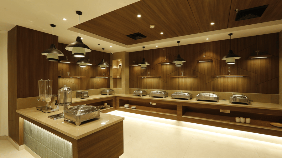 An image of a buffet hall featuring several covered utensils placed on the counter top and there are ceiling lights hanging from top - Tulip Inn, Zirakpur