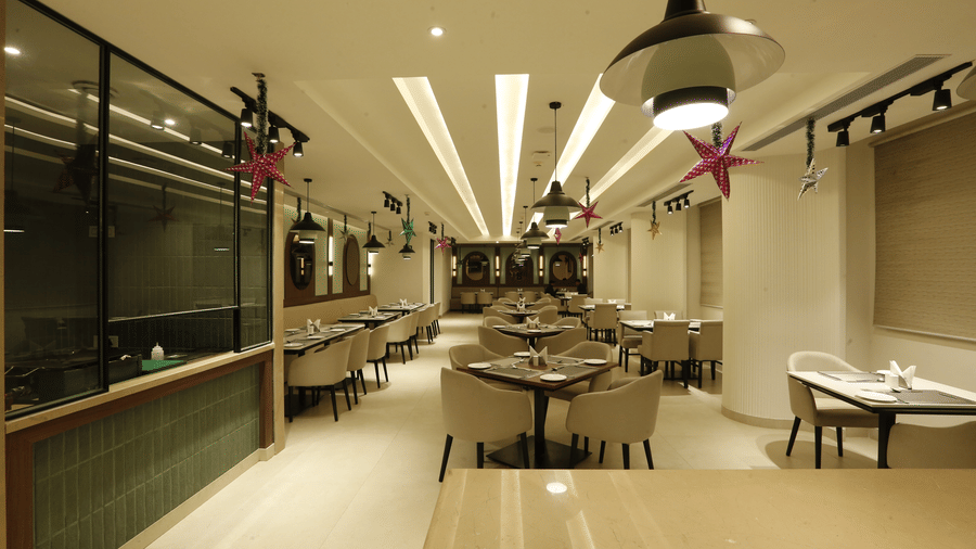 An image of a restaurant with several sets of table and chairs, lights installed on the ceiling, stars hanging from the ceiling, and there is also a counter at one side of the room - Tulip Inn, Zirakpur