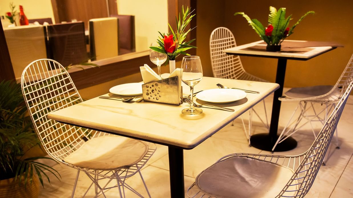 Wine and flower vase kept on table with white chairs arranged for two people