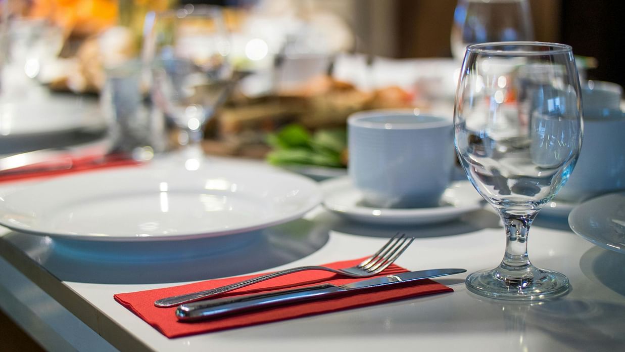 A dining table set with white plates, cutlery and empty wine glasses.
