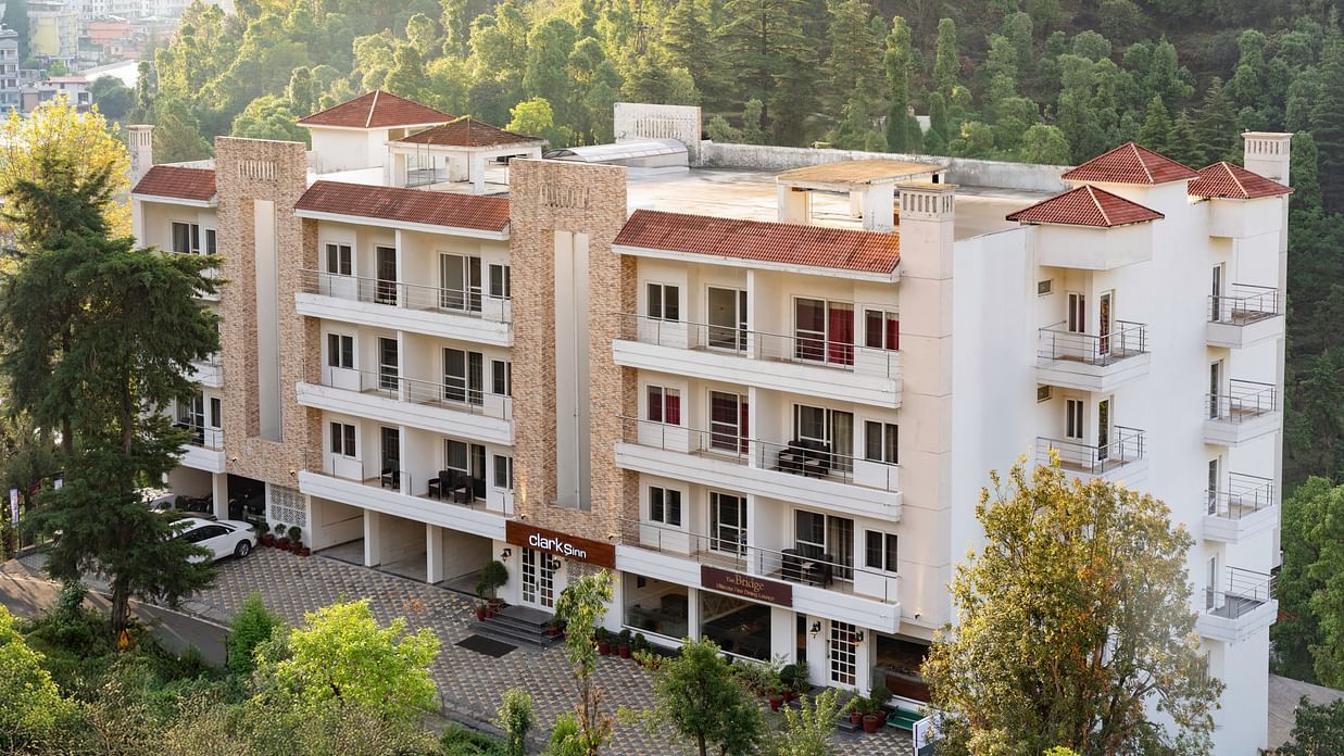 Facade of Clarks Inn, Near Kainchi Dham in Bhowali, nestled amongst trees with a view of surrounding hills.