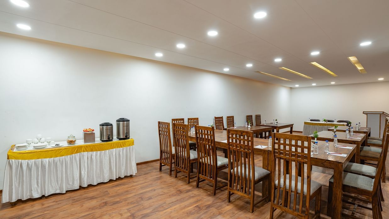 A well-lit conference room features wooden tables and chairs, a buffet area with drinks, and stationery laid out for attendees at Clarks Inn, Near Kainchi Dham.
