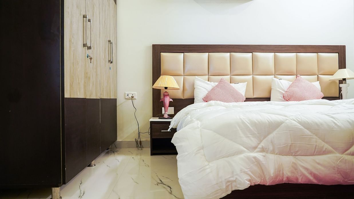 An image of a bedroom featuring a double size bed, a bedside table with lamp, and a wardrobe - Lime Tree 2BHK Service Apartment Near Artemis Gurgaon