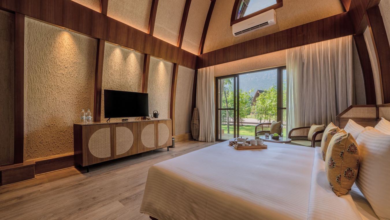 An image of a bedroom with double size bed, flat TV screen with table counter top, and a large window on one side of the room - Ananta Spa and Resort, Ajabgarh