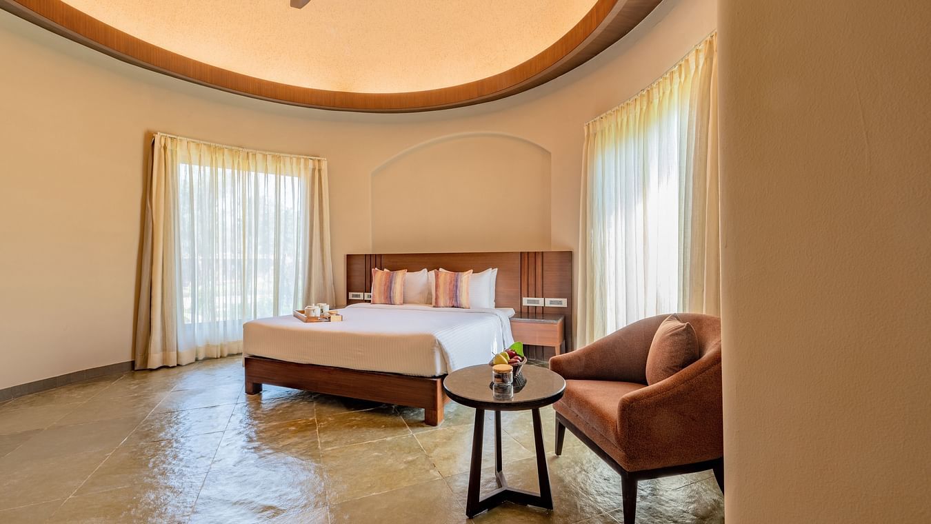 An image of a bedroom with a king size bed, a sofa with tea table, and two large windows with drawn curtains - Ananta Spa and Resort, Ajabgarh