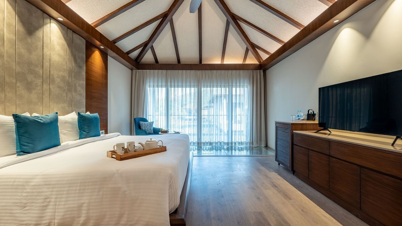 A image of a bedroom with a king size bed, a tea tray placed on it, a flat TV screen with counter top table, and a large window on one side  of the room - Ananta Spa and Resort, Ajabgarh