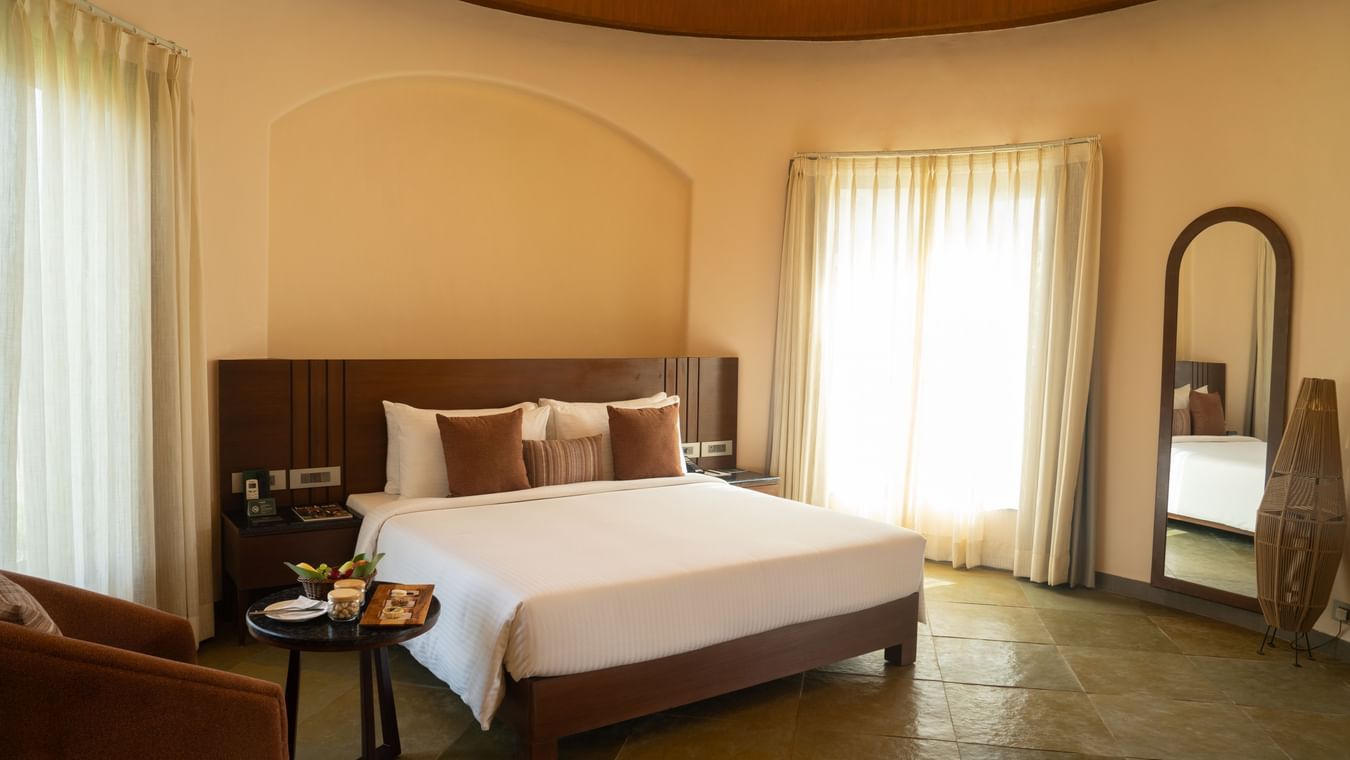 A warm bedroom with a double bed, soft lighting, and full-length mirror near the window at Ananta Spa and Resort, Ajabgarh.