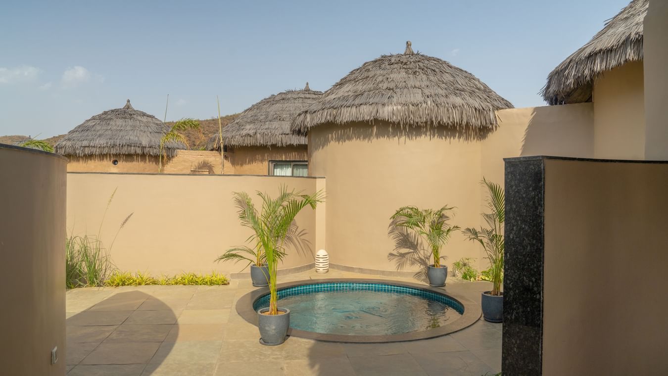 An outdoor view of a circular private plunge pool enclosed by rustic thatched-roof cottages at Ananta Spa and Resort, Ajabgarh.