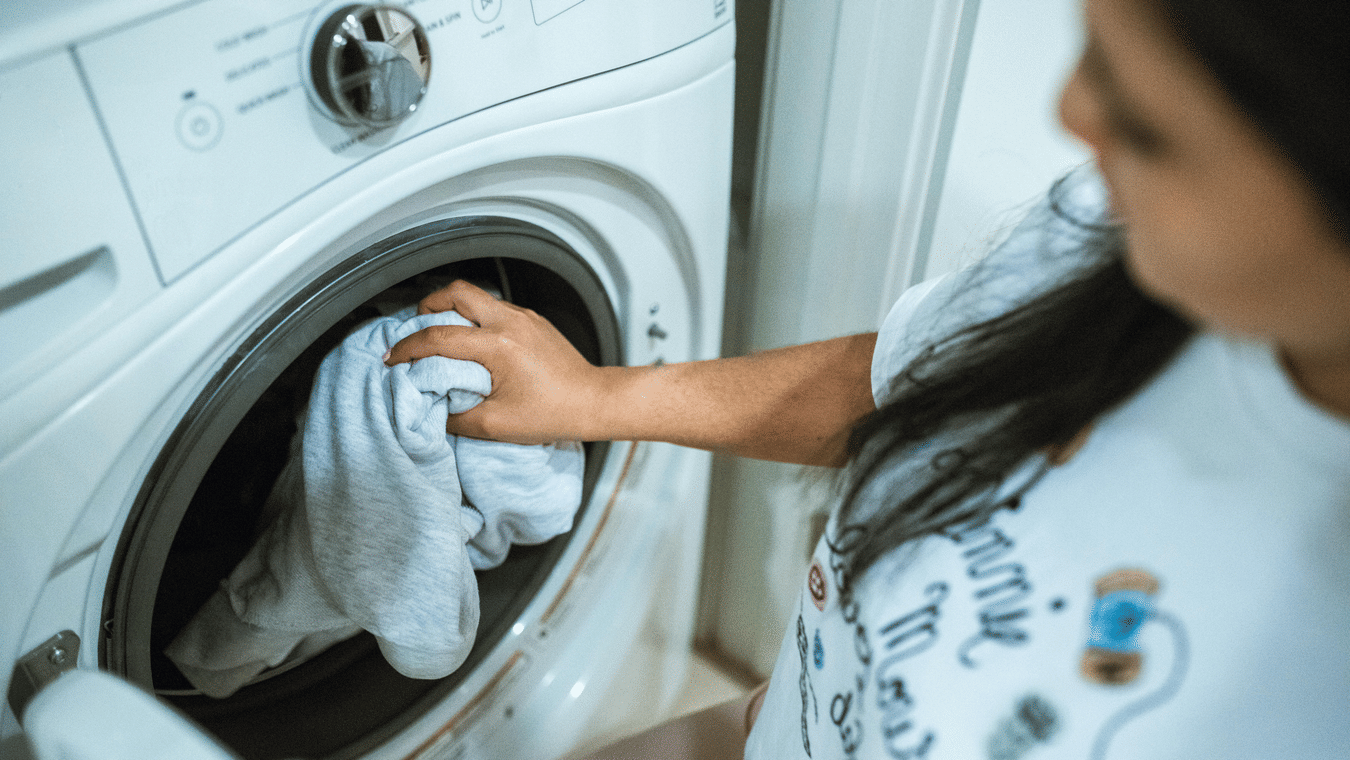 A woman putting a white cloth into a front-loading white washing machine.
