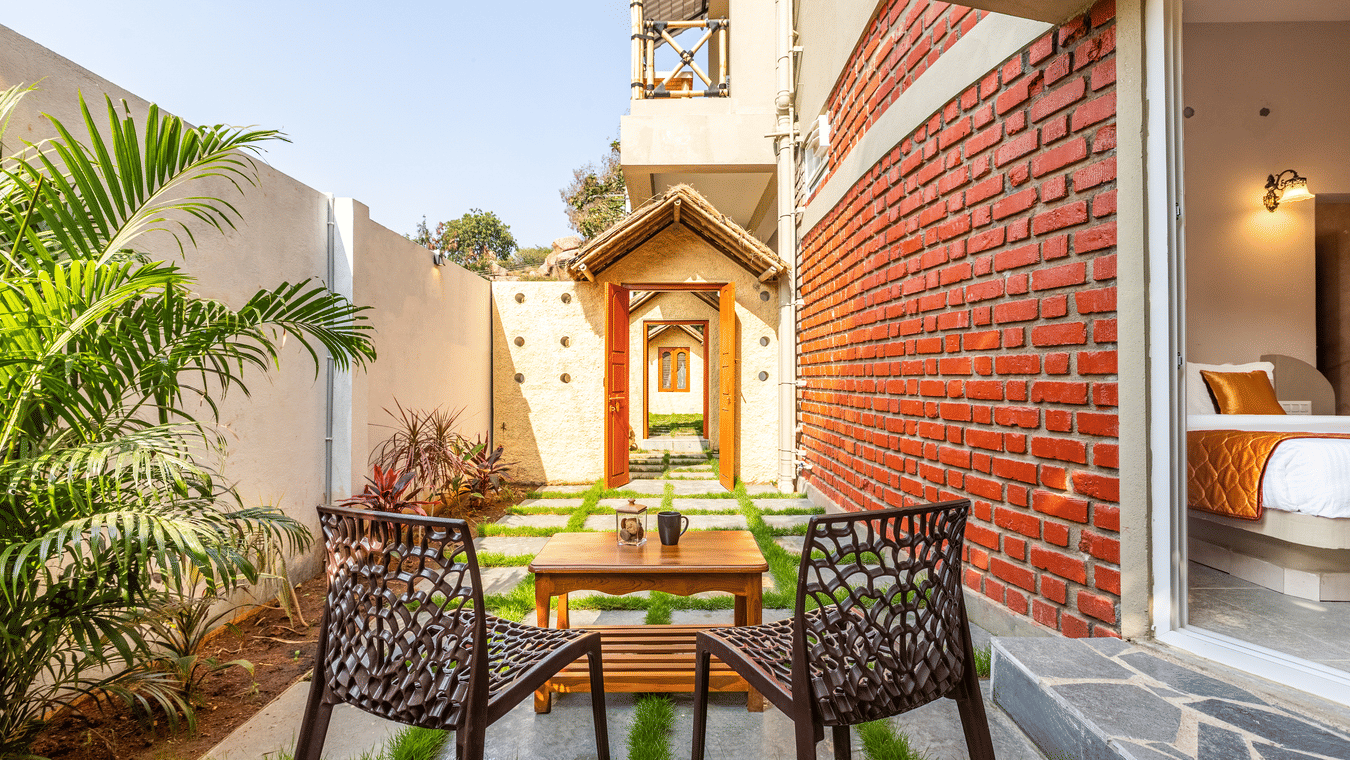 Small private outdoor courtyard with two wicker chairs and a table on a manicured lawn - Nature Trails Ashoka Resort Hampi