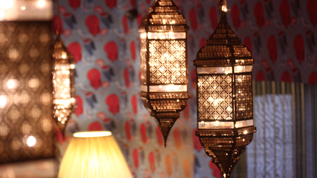 Intricately carved brass lanterns glowing with warm light against a vibrant patterned wallpaper backdrop.