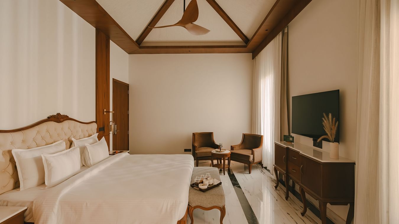 A side angle view of the bed at The Ananta, Udaipur with a bed, flat screen TV, seating area with two area.