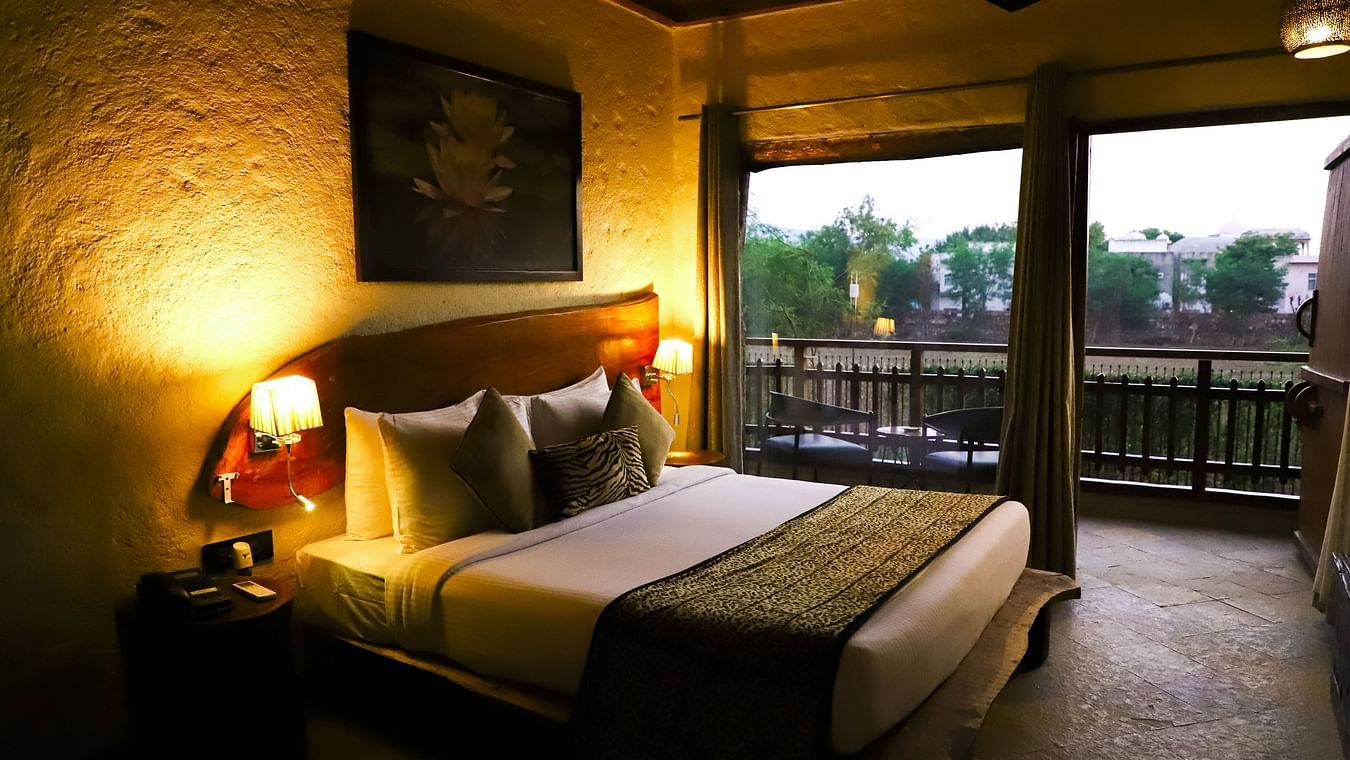 A bedroom with full-height windows, medieval looking walls and lamps on either side of the bed