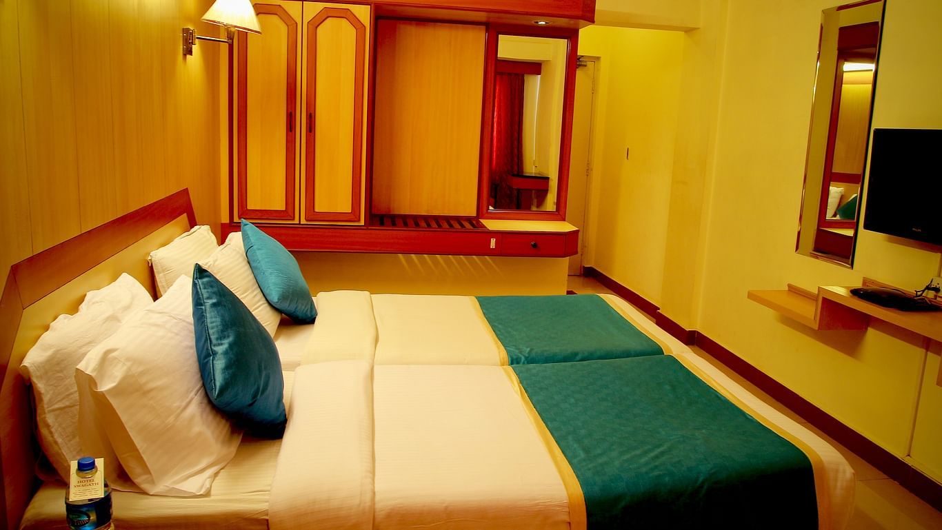 a room displaying a bed covered in white bed sheet and a wardrobe placed beside it - Hotel Swagath, Bangalore