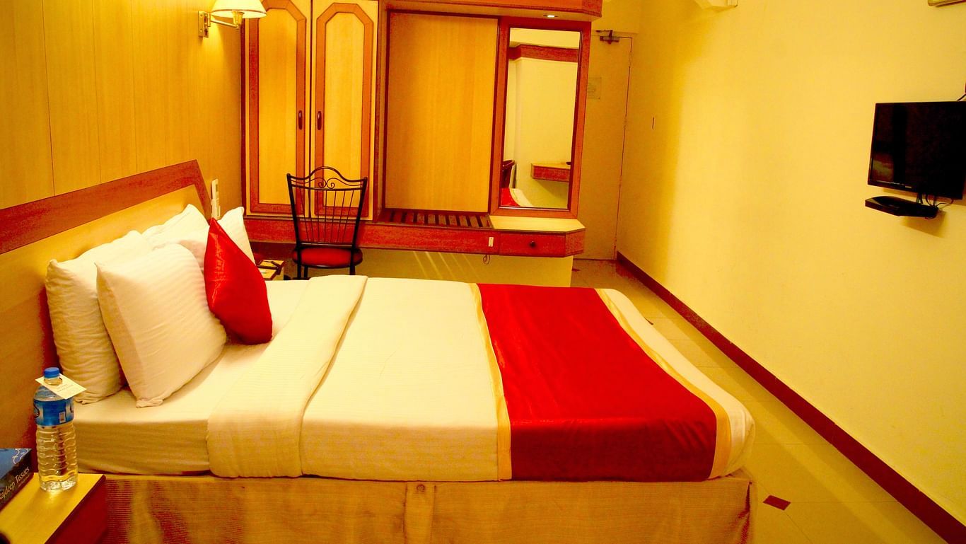 a side view of a room furnished with a comfortable bed, television, wardrobe and looking glass - Hotel Swagath, Bangalore