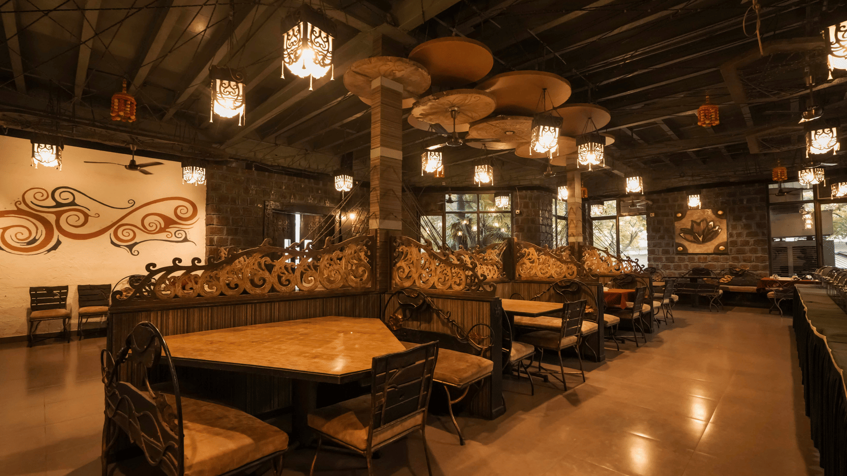 Interior view of a dark, ambient dining hall featuring high-backed booths and elaborate ceiling decorations at Adamo The Village.