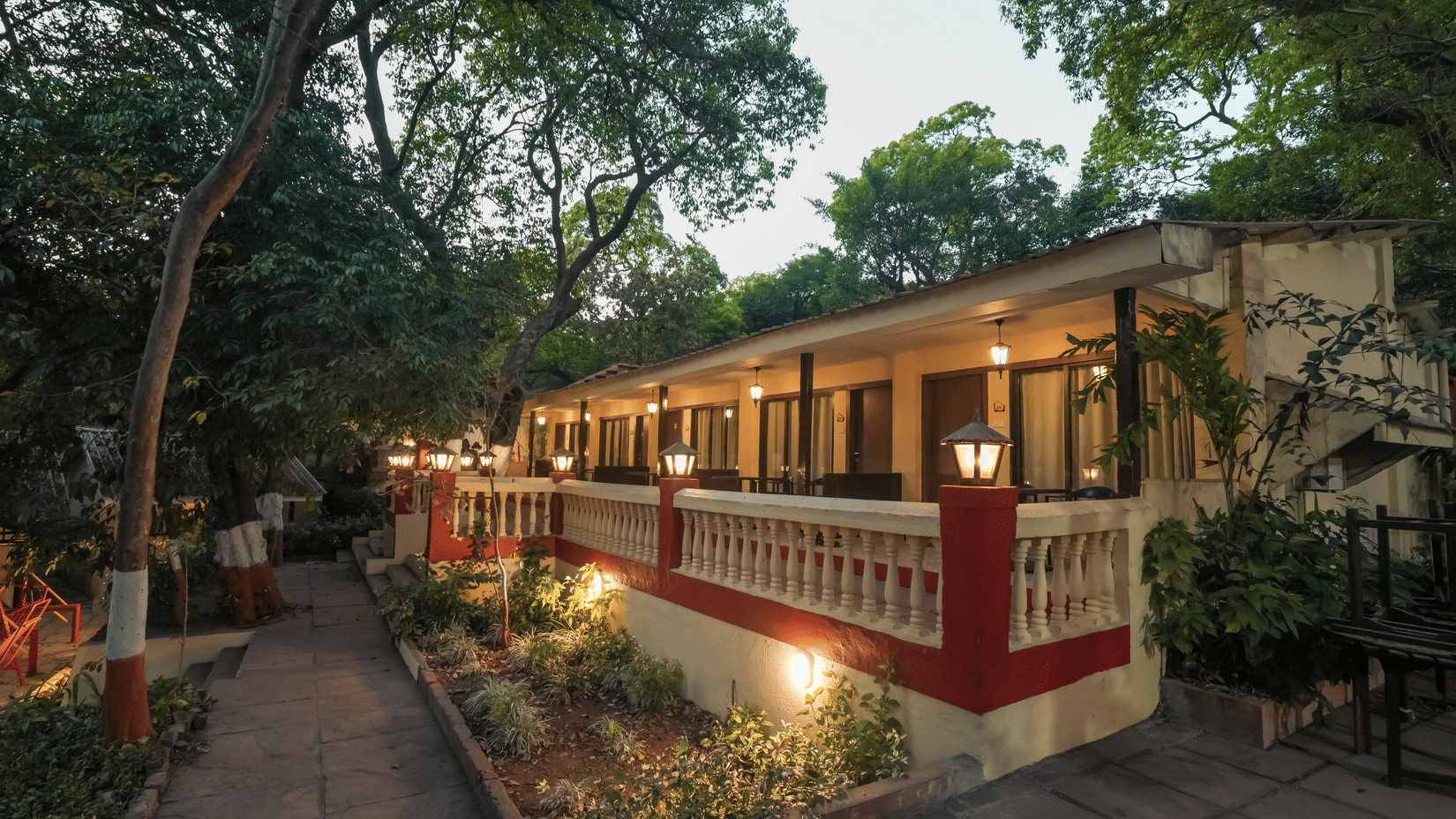 Exterior view of a resort property at dusk with warm lighting illuminating the pathways, garden, and building balconies.