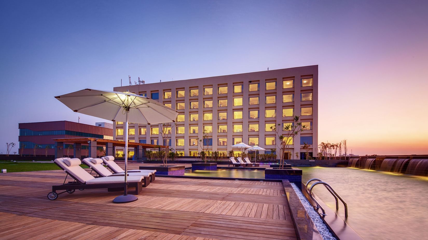 A hotel with a poolside area featuring lounge chairs, umbrellas, and a scenic sunset backdrop - Balaji Sarovar Premiere, Solapur