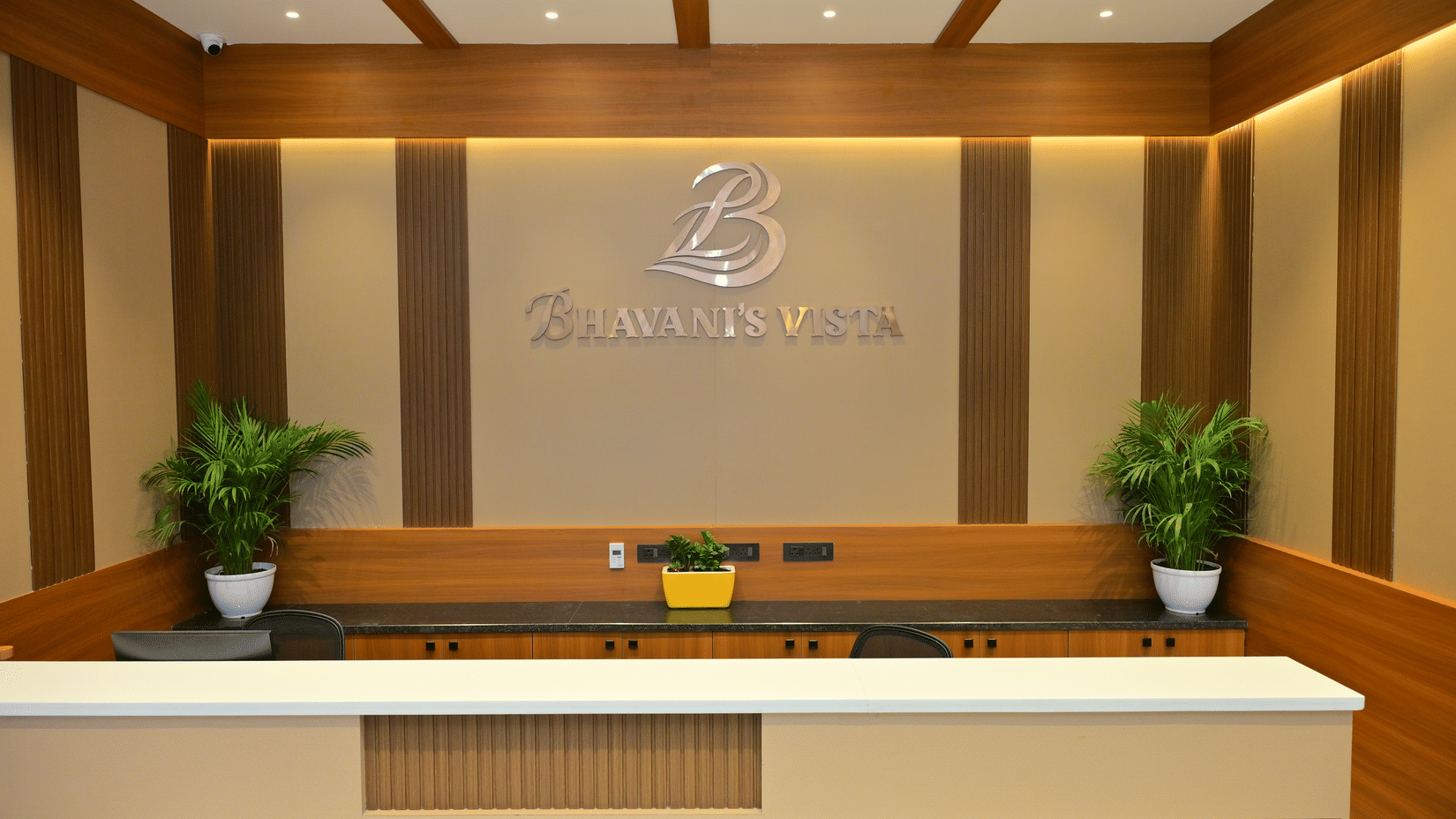 Reception desk of Bhavanis Vista By Icon featuring a counter, signage, and potted plants.