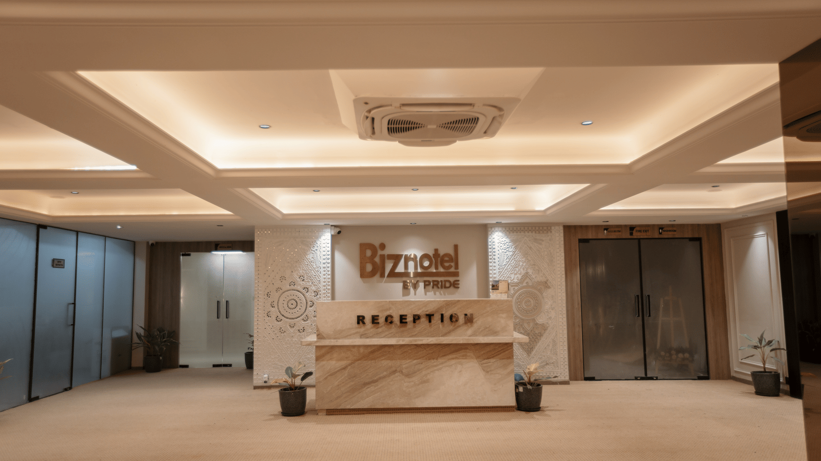 Elegantly lit reception counter and main lobby area at Biznotel by Pride Surat featuring warm coffered ceiling lighting.