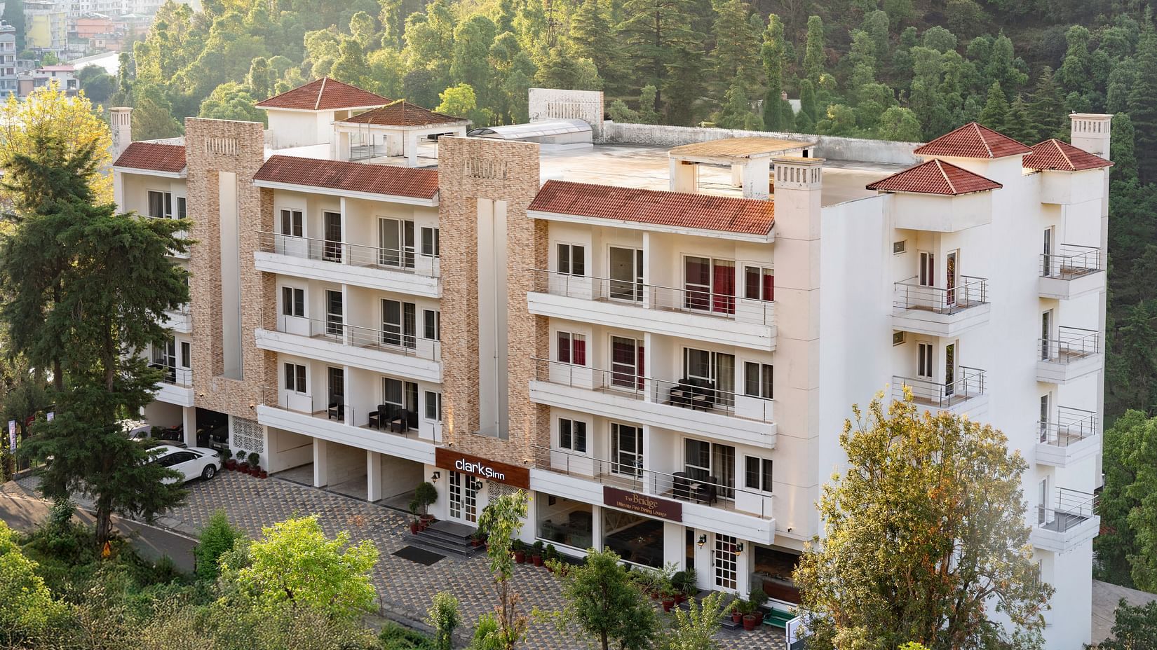 Facade of Clarks Inn, Near Kainchi Dham in Bhowali, nestled amongst trees with a view of surrounding hills.