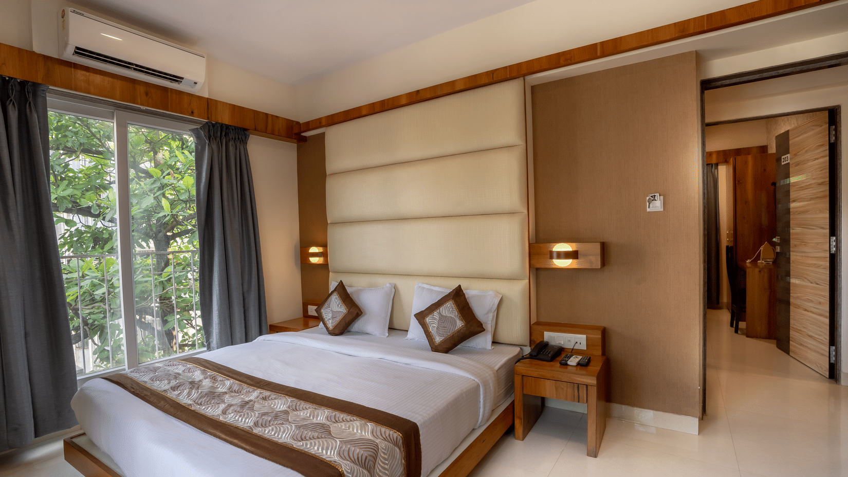 Bedroom featuring a plush bed next to the glass door to the balcony with an air-conditioner over it at Home2 Suites & Service Apartments for a pleasant stay near Mumbai Airport