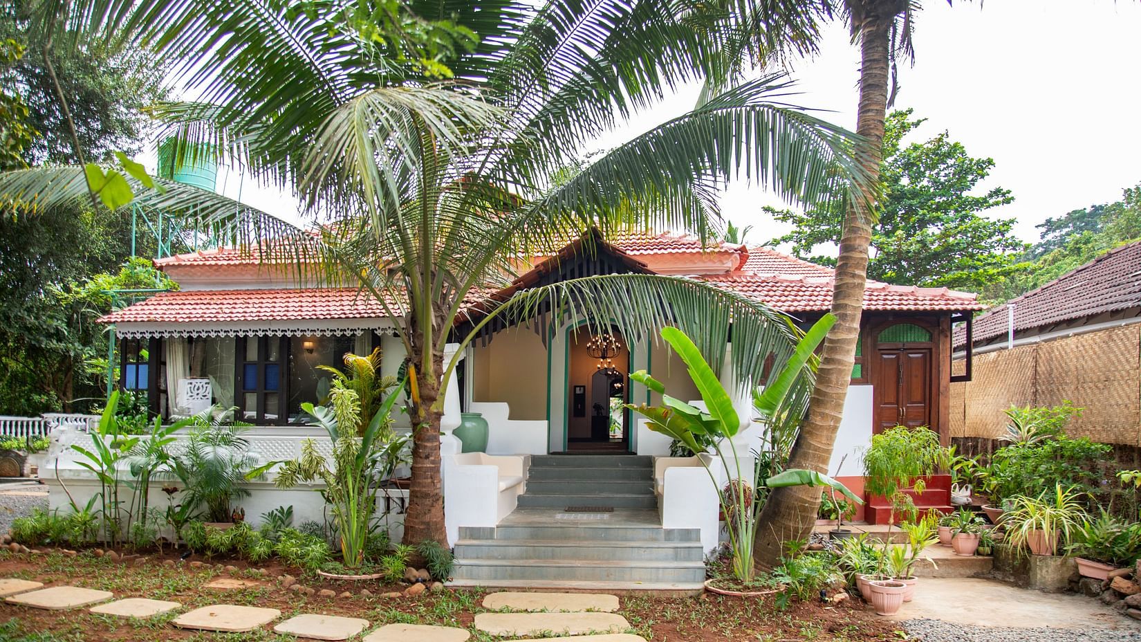 An image of a cottage style bungalow at Lamrin Ucassaim Hotel, Goa which is surrounded by palm trees