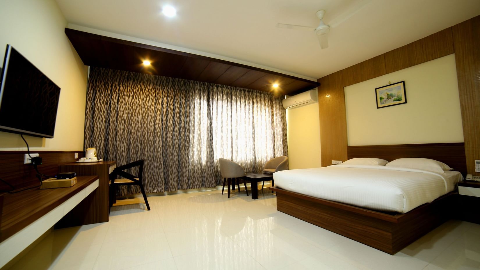 A room with neat bed sofa chairs and study desk and a TV - Mysore Gate Hotel Bangalore