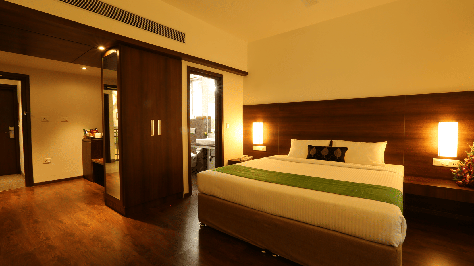 A spacious Executive Room featuring a bed with green runner, dark wood panelling, warm bedside lights, and wooden flooring at Temple Tree Hotel, Bangalore.