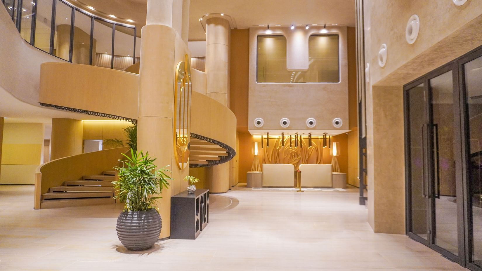 Expansive, sunlit hotel lobby with soaring ceilings, a graceful curved staircase, and lush green potted plants creating a welcoming atmosphere - The Orchid Hotel, Chandigarh
