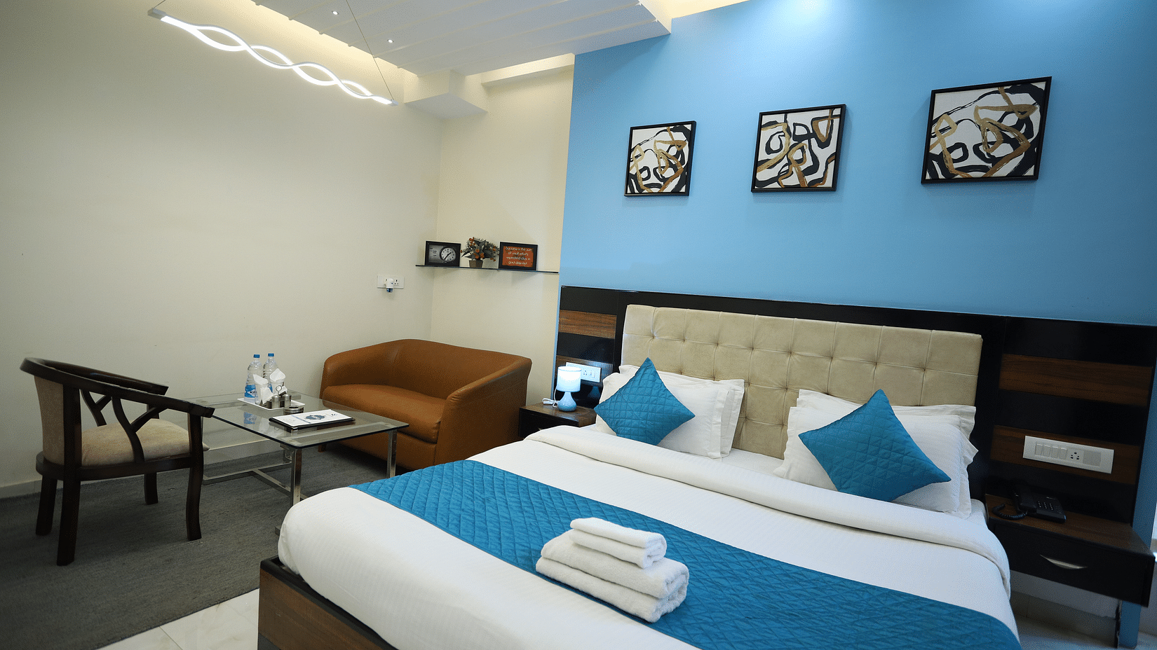 A hotel room with a bed, seating area, and wall decorations - Asian Suites Cyber Park, Gurgaon.