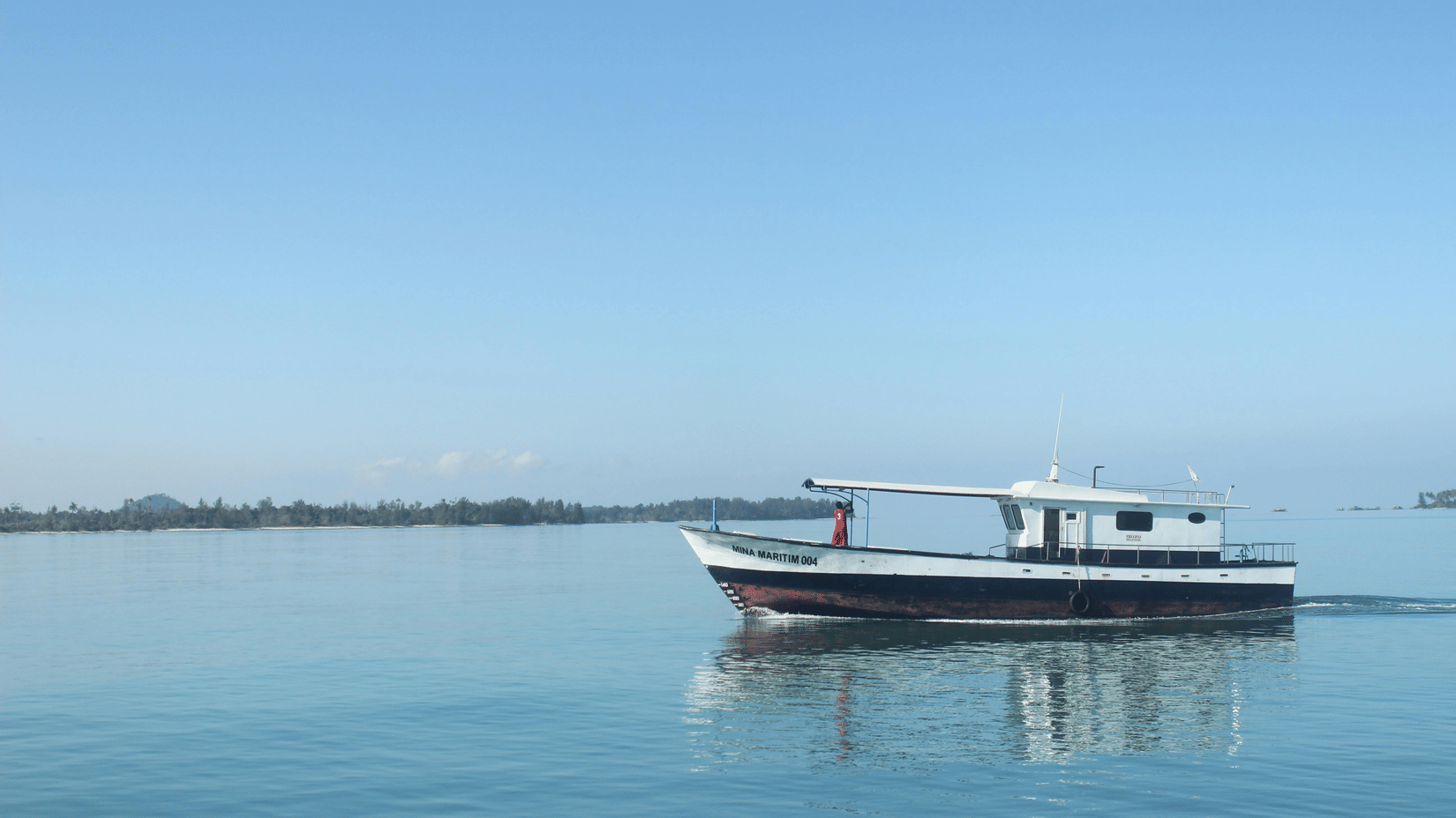 A small motorized boat traveling across a calm, open body of water under a clear sky.