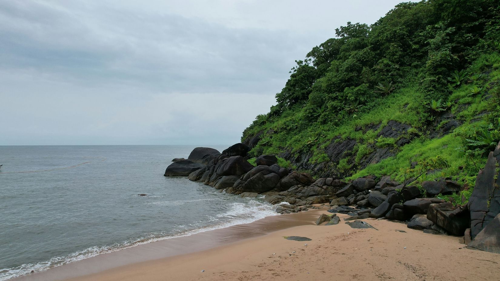 An overview of Butterfly Beach with a hill next to the coastline and cloudy sky in the background.