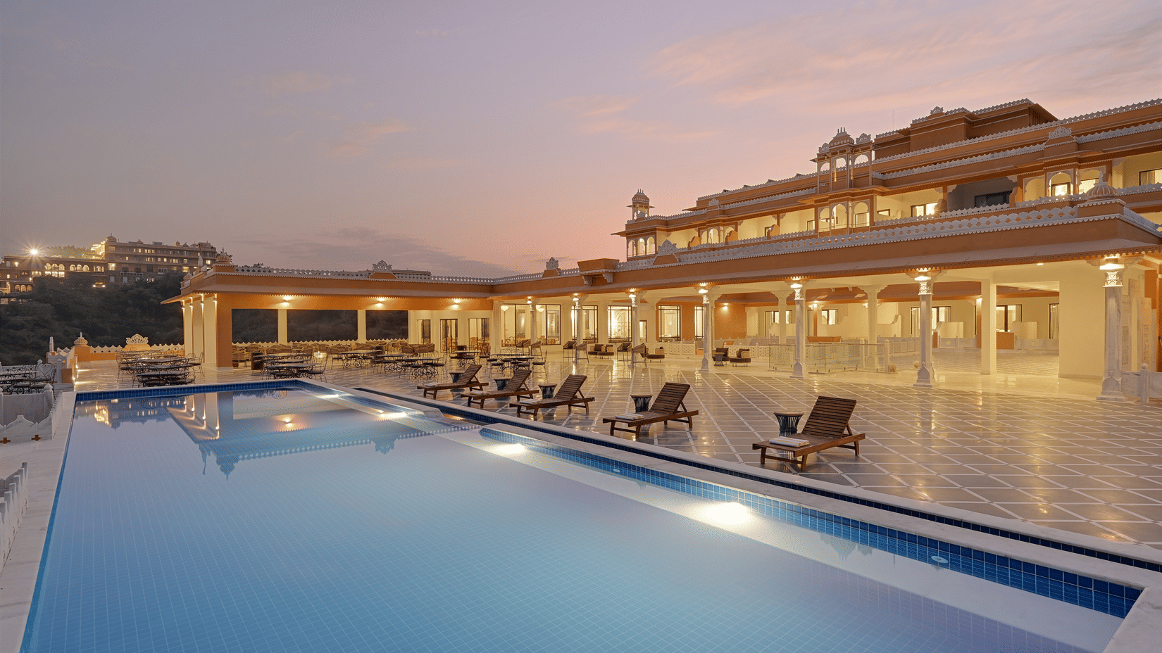 Facade of Fateh Vilas in Udaipur featuring a well lit building and a swimming pool.