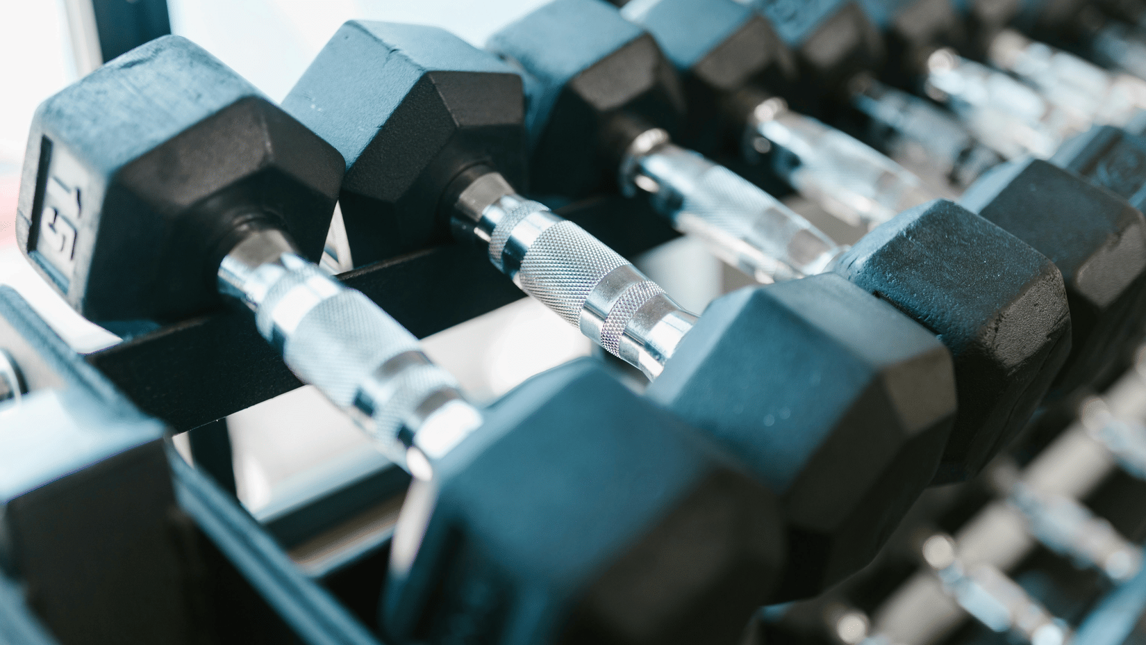 Close-up of black hex dumbbells with chrome handles neatly arranged on a rack in a fitness centre, highlighting strength training equipment in a gym setting.
