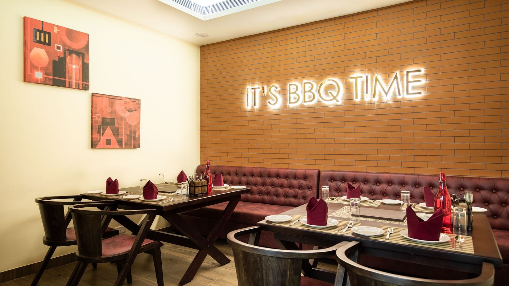 A restaurant with dark wooden tables, chairs, and a neon sign that reads ITS BBQ TIME on a textured wall - Jenneys Residency, Coimbatore