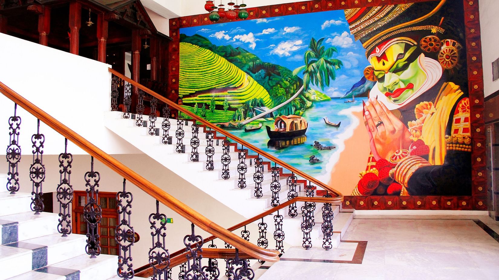 Staircase with ornate railing beside a vibrant Kathakali mural and tropical scenery - Jenneys Residency, Coimbatore