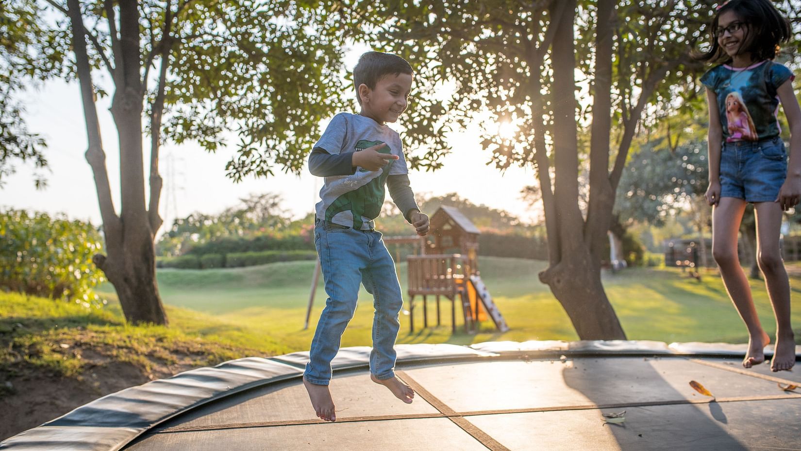 children jumping on a trampoline with trees and the sun set in the background - Karma Lakelands