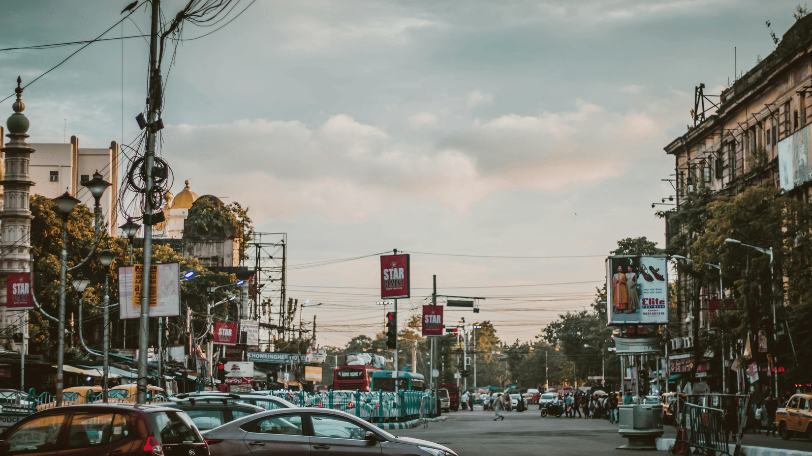 A busy city street scene is shown with cars, trams, and buildings under a cloudy sky.