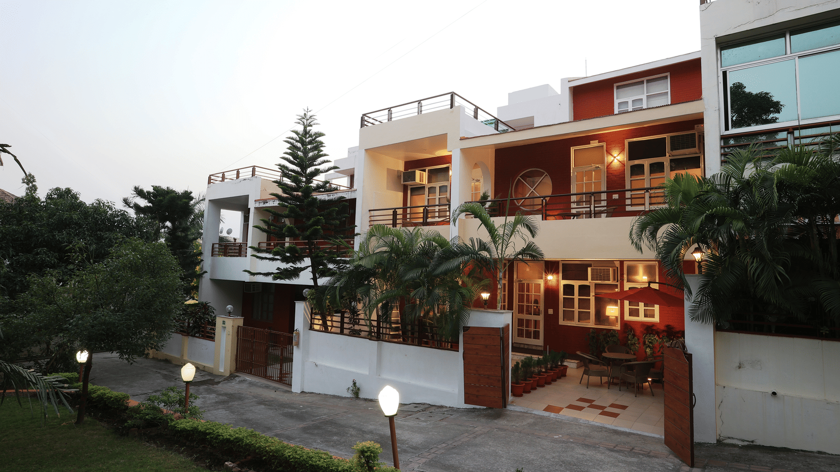 A facade image of a two storey building surrounded by trees and there are also lights beside the pathway to the entrance gate - Lamrin Boutique Cottages Rishikesh