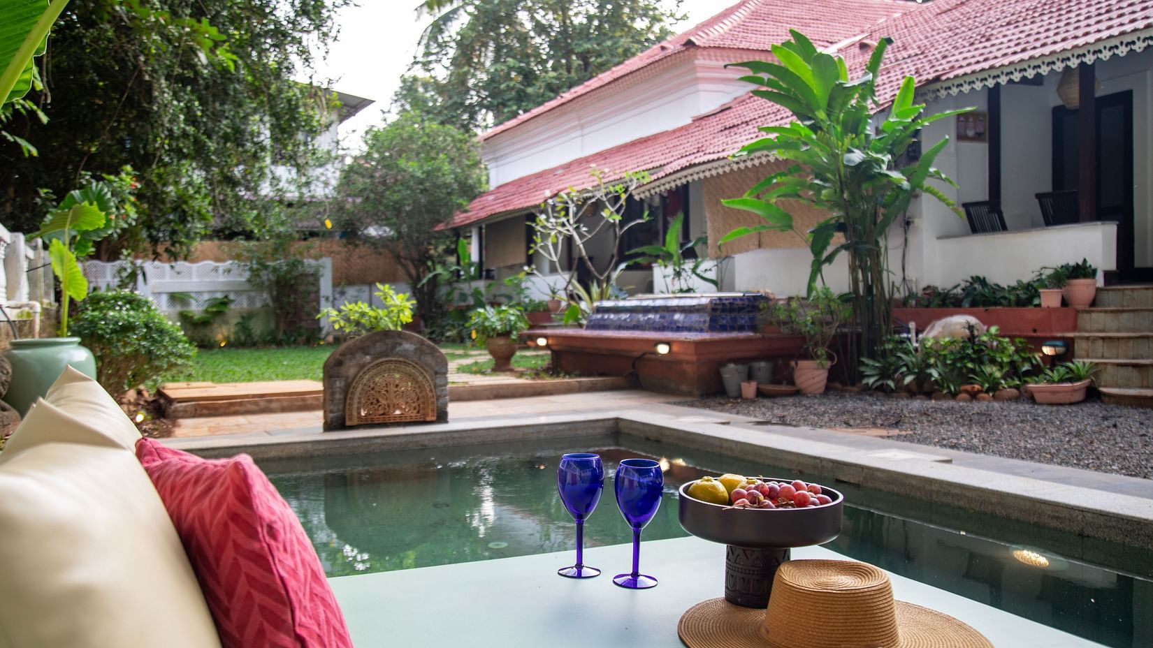L shaped pool side with two blue wine glasses and surrounded by greenery @ Lamrin Ucassaim Hotel, Goa