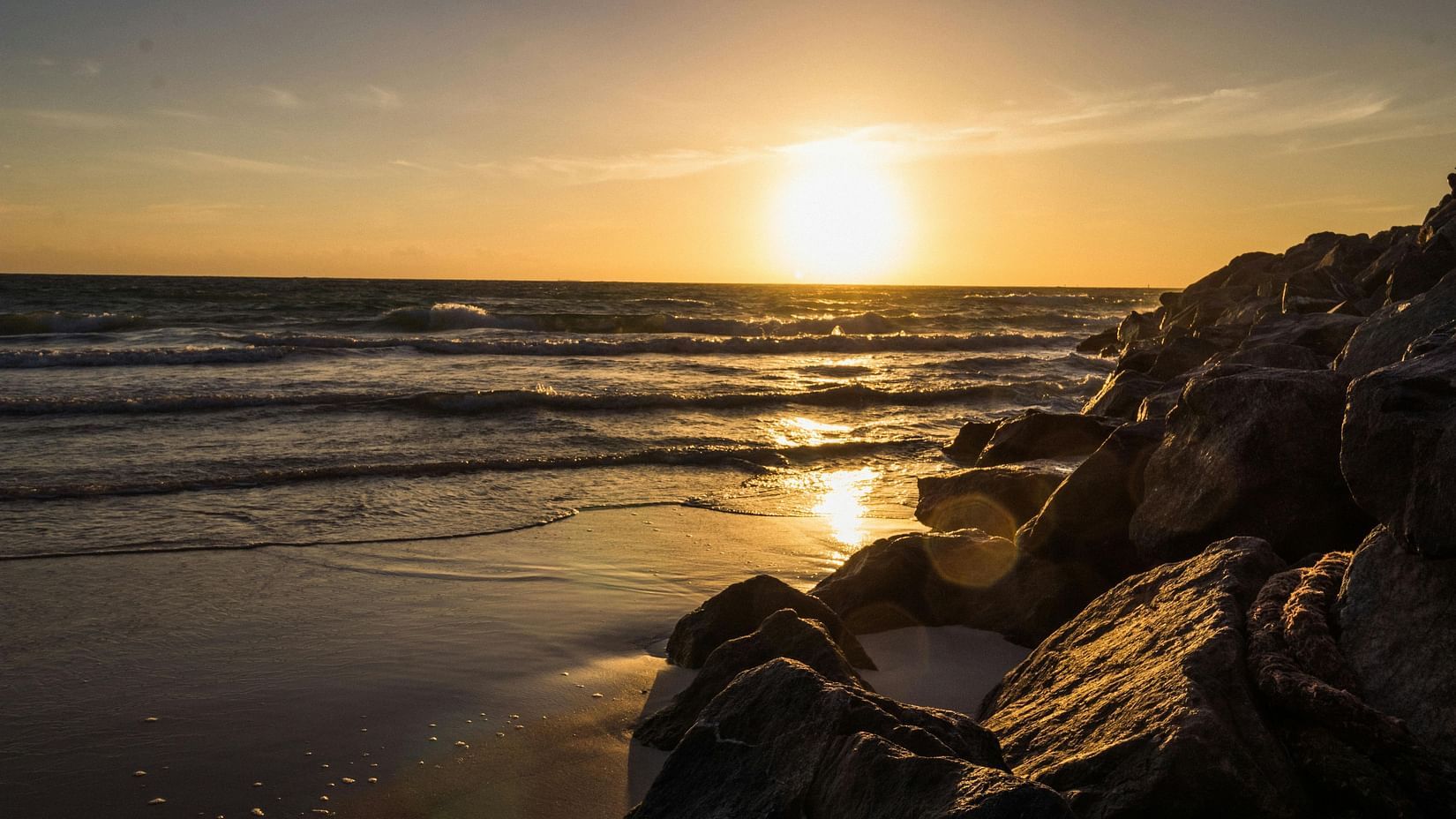 Sunset over a beach with vibrant hues of yellow reflecting on the water