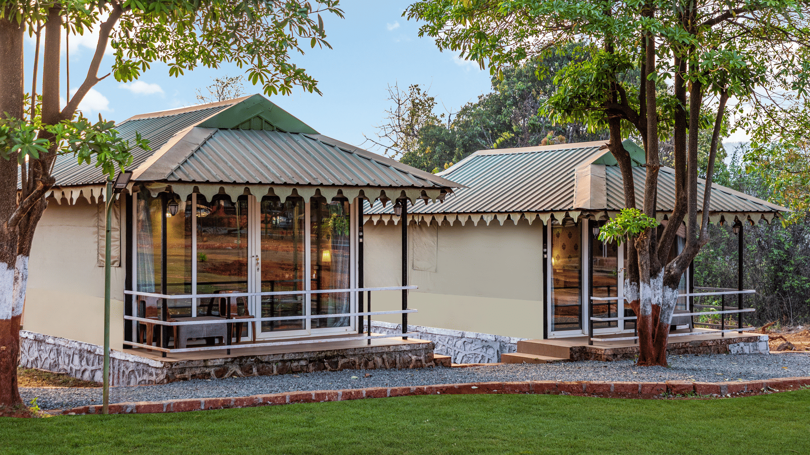 Nature Trails Kudalika two cream-coloured Swiss-style cottages with green corrugated roofs, large glass frontage, stone base, private decks and surrounding trees.