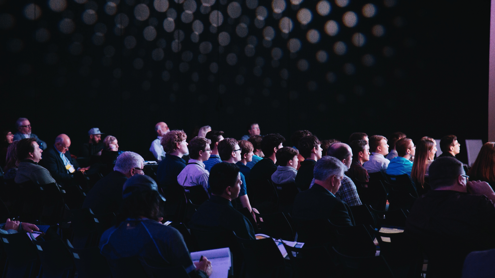 A dim-lit conference hall with people attending a symposium