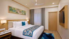 a double bed, rug, television painting and bedside tables in a Premium Cottage at ABN Sarovar Portico, Jim Corbett