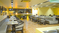 A restaurant dining room at Ambar Sarovar Portico, Gandhidham features neatly arranged tables, chairs, and cushioned booth seating along the wall.