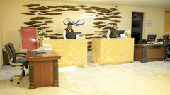 2 receptionists work behind wooden front desks in the reception lobby area at Ambar Sarovar Portico, Gandhidham featuring a wall art display.