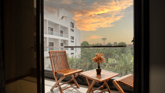 Hotel room balcony with wooden chairs and a table overlooking the surrounding area at sunset at Arawali Ananta Elite, Jaipur.