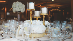 A formal table setting at an event, featuring a centrepiece with tall candles in gold holders and clear drinking glasses with water.